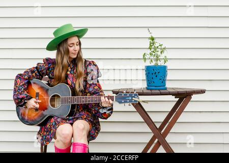 Eine schöne Frau sitzt an einem Tisch im Freien und spielt eine Akustische Gitarre Stockfoto