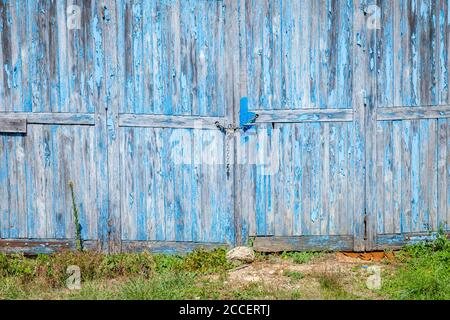 Verwitterte Garagentür mit abblätternder blauer Farbe, die mit einem verschlossen war Kette Stockfoto