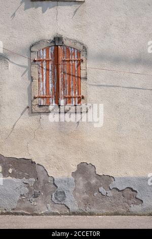 Fenster in einer verwitterten Gipsfassade mit braunen Holzfenstern Und abblätternde Farbe Stockfoto