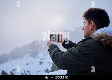 Ein junger latein macht ein Foto mit seinem Handy Umgeben von Schnee Stockfoto