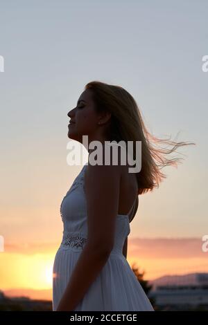 Die junge Frau schließt die Augen, während der Wind sie streichelt Blick bei Sonnenuntergang Stockfoto