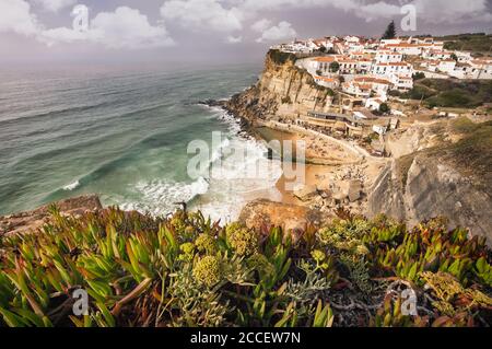 Sommerurlaub im schönen Azenhas do Mar Stadt. Netter Strand, weiße Kreidehäuser an einem Klippenrand. Bly Himmel mit weißen Wolken und grünen Laub im Vordergr Stockfoto