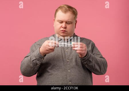 Morgendliches Routinekonzept. Verdächtiger skeptischer Mann hält Zahnbürste in der Hand, kurvt Lippen, kümmert sich um die Gesundheit und Hygiene seiner Zähne, trägt lässige gre Stockfoto