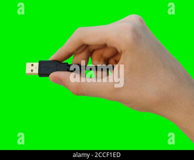 Nahaufnahme männliche Hand hält schwarzes usb-Kabel für PC und mobile Geräte isoliert auf grünem Hintergrund, Konzept der Menschen Kommunikation. Stockfoto