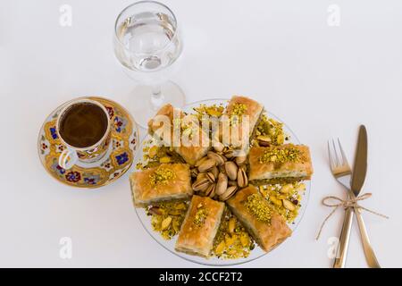 Traditionelle türkische Konditorei Dessert Pistachio Baklava auf weiß mit türkisch Kaffee, Besteck und ein Glas Wasser Stockfoto