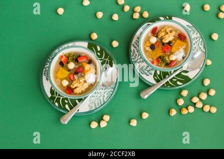 Traditionelles türkisches Dessert Ashura oder Noah's Pudding in stilvollen grünen Schalen auf grünem Hintergrund mit Haselnüssen. Stockfoto