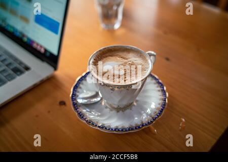 Heißer Aroma Cappuccino Kaffeetasse auf Holztisch Arbeit von zu Hause mit Laptop, Home Business WFH Konzept Stockfoto