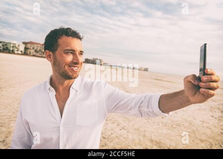 Selfie Urlaub Strandmann in weißem Leinen Shirt fotografieren mit Handy auf Hochzeitsreise Urlaub. Glückliche junge mit Smartphone auf holdiay Stockfoto