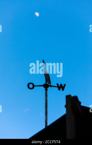 Der verschwommene Mond am blauen Himmel, im Vordergrund ein Wetterhahn Stockfoto