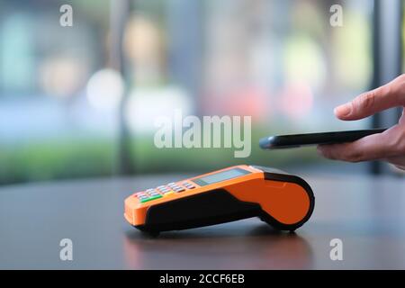 Nahaufnahme Menschen mit Smartphone zu zahlen über POS-Terminal auf dem Schalter. Bunte Bokeh Hintergrund Stockfoto