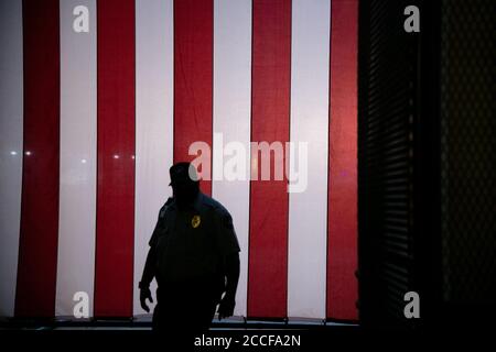 Ein Sicherheitsbeamter geht an einer riesigen amerikanischen Flagge vorbei, die in Woodrow Wilson Plaza hinter einem temporären Metallzäuning vor der Republikanischen Nationalversammlung von 2020 in Washington, DC, am 21. August 2020 inmitten der Coronavirus-Pandemie. Präsident Trump wird die republikanische Nominierung für den Präsidenten vom South Lawn des Weißen Hauses akzeptieren, da andere Kongressveranstaltungen auch auf Bundeseigentum stattfinden C-Ethik-Experten haben Bedenken geäußert, dass dies möglicherweise Bundeskorruptionsgesetze verletzt, die die Verwendung von Regierungseigentum und Mitarbeitern für einschränken Politische Aktivitäten. (Graeme Sloan/Sipa Stockfoto