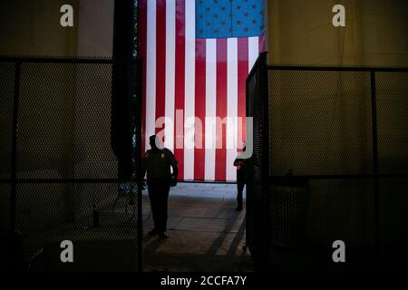 Die Sicherheitsbeamten gehen an einer riesigen amerikanischen Flagge vorbei, die in Woodrow Wilson Plaza hinter einem temporären Metallzaun vor der Republikanischen Nationalversammlung von 2020 in Washington, DC, am 21. August 2020 inmitten der Coronavirus-Pandemie. Präsident Trump wird die republikanische Nominierung für den Präsidenten vom South Lawn des Weißen Hauses akzeptieren, da andere Kongressveranstaltungen auch auf Bundeseigentum stattfinden C-Ethik-Experten haben Bedenken geäußert, dass dies möglicherweise Bundeskorruptionsgesetze verletzt, die die Verwendung von Regierungseigentum und Mitarbeitern für einschränken Politische Aktivitäten. (Graeme Sloan/Sipa Stockfoto