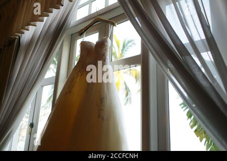 Ein schönes weißes Hochzeitskleid, das neben einem Fenster hängt Stockfoto