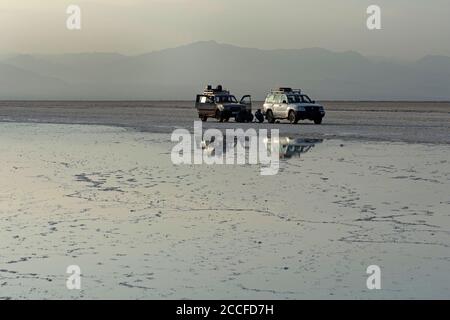 Zwei Allradfahrzeuge stehen im hellen Abendlicht vor einer Sole am Rande des Assale Salt Lake, Hamedala, Danakil Valley, Afar R Stockfoto