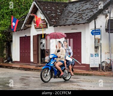 Zwei Frauen mit einem Regenschirm auf einem Moped Fahrt im Regen, Luang Prabang, Laos Stockfoto