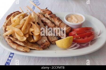 Traditionelle griechische Küche. Portion Souvlaki mit Bratkartoffeln, Tomaten, Zitrone und einem Topf Stockfoto