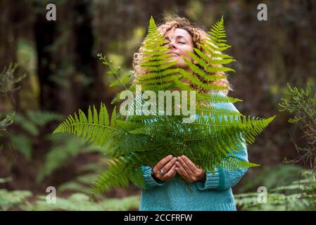 Tag der Erde und Liebe für die Natur Konzept mit schönen Frau Mit geschlossenen Augen fühlen Sie das große Blatt und genießen Sie die Outdoor natürliche Freizeitaktivitäten - sparen Stockfoto