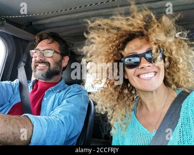 Fröhliches Paar fahren und genießen Sie die Fahrt in einem Auto Mit Wind im Haar - schöne junge Frau lächeln An der Kamera - Menschen reisen auf Fahrzeug con Stockfoto