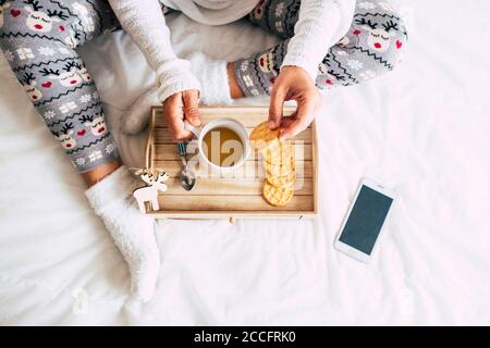 Blick von oben auf die kaukasische Frau, die im Bett frühstückte Eine weiße Abdeckung - Fensterdekorationen und Themen - weiß Hintergrund und weihnachten Saison Lifestyle con Stockfoto