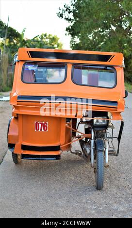 Ein leeres orangefarbenes Dreirad ist an einer Betonstraße in Coron, Palawan, geparkt Stockfoto