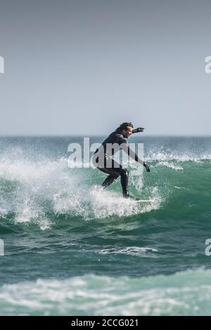 Ein Surfer auf dem Kamm einer Welle, die links bei Fistral in Newquay in Cornwall bricht. Stockfoto