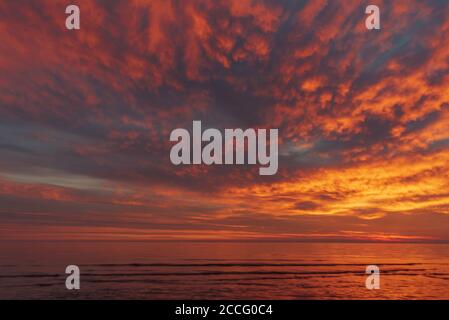 Der Moment nach Sonnenuntergang, wenn die Sonne hinter dem Horizont verschwunden ist und die Wolken und die Wasseroberfläche in interessanten rötlich-orangen s färbt Stockfoto