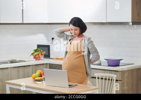 Junge schwangere Frau leidet unter Kopfschmerzen im Home Office Stockfoto