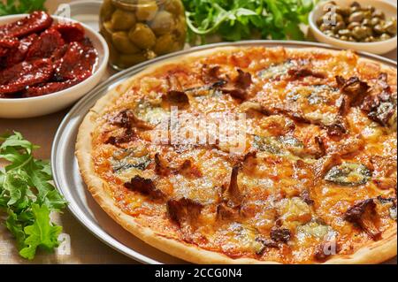 Pizza mit Pilzen, Käse, Basilikumblättern auf einer Aluminium-Pizzapfanne. Frische Rucola, Oliven, getrocknete Tomaten und Kapern Stockfoto