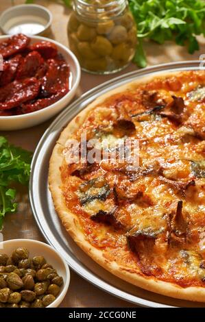 Pizza mit Pilzen, Käse, Basilikumblättern auf einer Aluminium-Pizzapfanne. Frische Rucola, Oliven, getrocknete Tomaten und Kapern Stockfoto