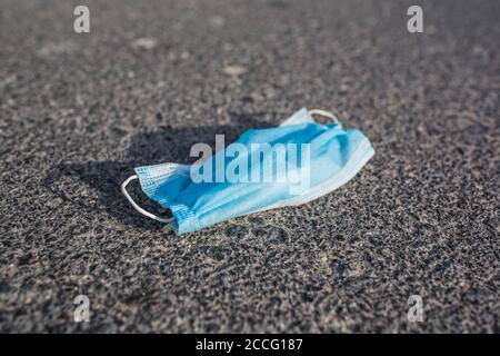 Gebrauchte medizinische Gesichtsmaske auf dem Bürgersteig einer öffentlichen Straße entsorgt. Umweltverschmutzung und Umweltverschmutzung während der Coronavirus-Pandemie. Stockfoto