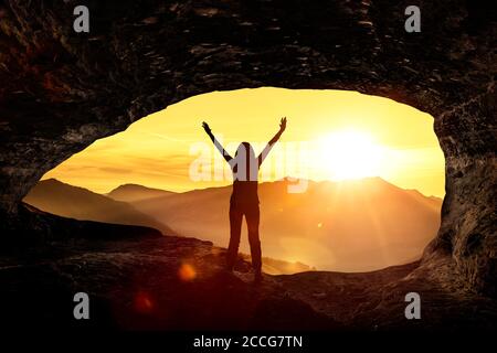 Silhouette einer Frau begrüßt den Sonnenaufgang in einer Höhle Stockfoto