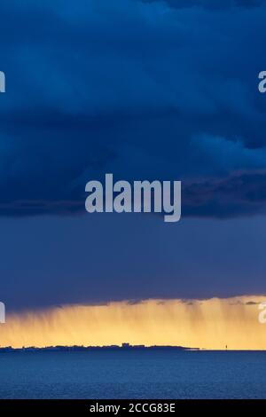 Europa, Deutschland, Niedersachsen, Otterndorf. Dunkle Sturmwolken über Cuxhaven, dahinter goldenes Abendlicht über der Außenelbe. Stockfoto