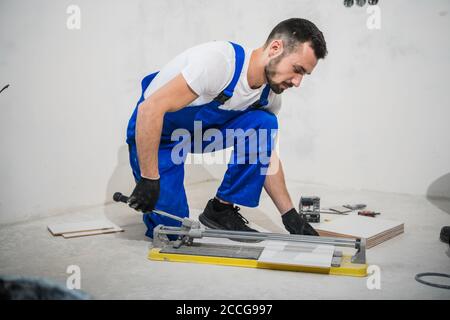 Der Generalarbeiter mißt die Fliesen und schneidet sie mit Eine Keramiksäge Stockfoto