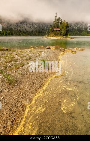 Gelber Pollen von Nadelbäumen driftet im Frühjahr am Ufer des Eibsee im Wettersteingebirge. Im Hintergrund eine kleine Insel mit einem Stockfoto
