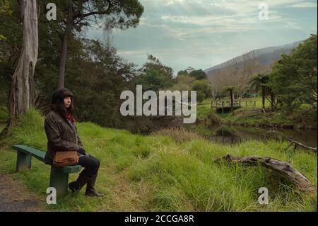 Tourist sitzt auf einer Bank am Ufer des jungen Yarra River im oberen Bereich des Yarra Valley im Land Victoria in Australien. Stockfoto