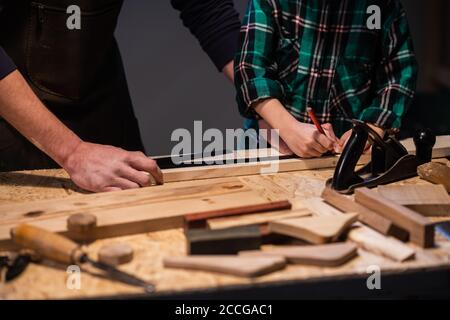 Nahaufnahme der Arbeit eines Mannes und eines Jungen am Tischlertisch, auf dem Tisch sind ein Flugzeug, Meißel, Brett, Werkbank, Lineal und andere Gegenstände Stockfoto