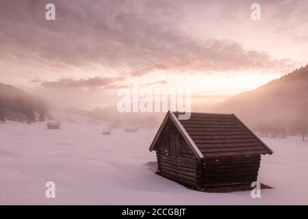 Morgenstimmung in den deutschen Alpen. Heuhaufen im dichten Nebel und die ersten Farben des Sonnenaufgangs, im Hintergrund die Sowendgruppe des Karwendels, im Fo Stockfoto