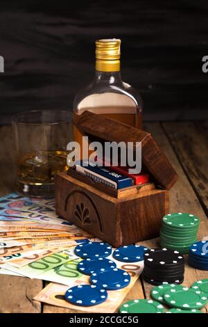 Vertikale Aufnahme eines Glases und einer Flasche Whiskey mit Karten, Geld und Pokerchips Stockfoto