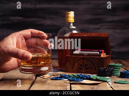 Die Hand der Person hält ein Glas Whiskey während des Pokerspiels Mit Chips auf dem Tisch liegen Stockfoto