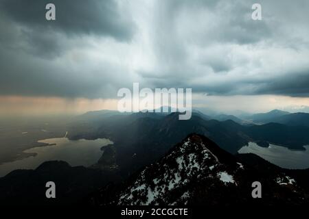 Herzogstand, Kochelsee und Walchensee im Frühjahr mit Schneeresten in Gewitterstimmung, leichtem Regen und Sonnenuntergang. Stockfoto