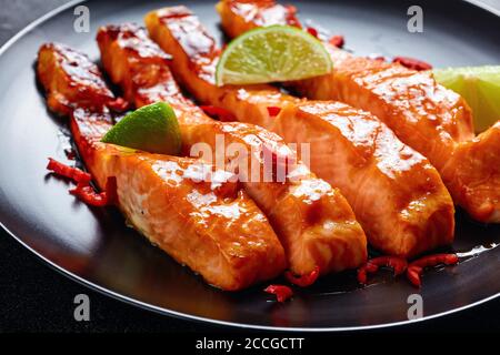 teriyaki Lachsfilet im Ofen gebacken, serviert auf einem schwarzen Teller mit Limettenkeilen auf einem Betontisch, horizontale Ansicht von oben Stockfoto