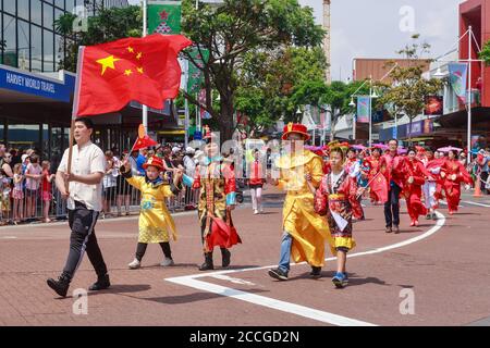 Chinesen in traditionellen Kostümen marschieren hinter der chinesischen Flagge die Straße hinunter. Aufgenommen bei einer Parade in Tauranga, Neuseeland, 11/30/2019 Stockfoto