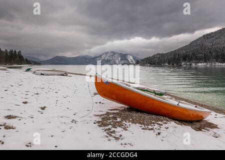 Wintereinbruch am Walchensee in den bayerischen Voralpen. Im Vordergrund ein Ruderboot und im Hintergrund der Herzogstand mit Schnee und Stockfoto