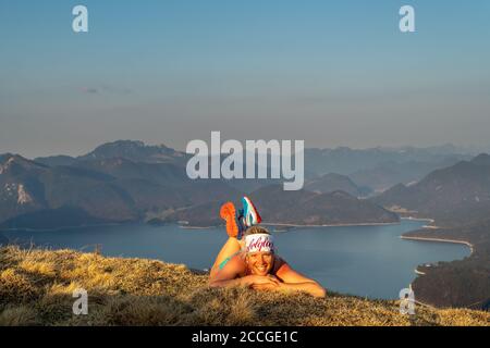 Trailrunnerin Katharina Kirschner liegt auf einer Frühlingswiese auf Simetsberg, im Hintergrund der Walchensee und lächelt die Kamera an. Stockfoto