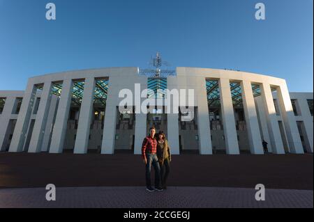 Ein Touristenpaar, das sich an einem klaren Wintertag vor dem Haupteingang des australischen parlamentshauses in Canberra umarmt. Stockfoto