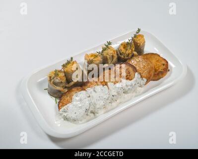 Fischkuchen mit weißer Soße und Fischfilet-Rollen, gefüllt mit Käse und Kräutern auf einem Teller auf weißem Hintergrund. Meeresfrüchte Stockfoto
