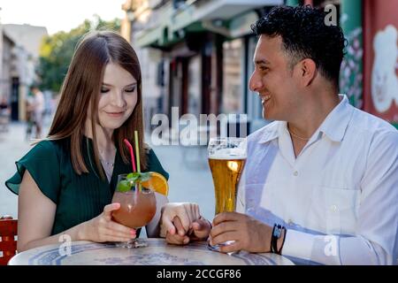 Multirassisches Paar auf einem ersten Termin auf der Straßenterrasse des Cafés. Freundschaftskonzept mit jungen, multiethnischen Menschen, die Zeit miteinander genießen. Stockfoto