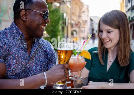 Multirassische Freunde trinken und toasten auf der Straßenterrasse des Cafés. Freundschaftskonzept mit jungen, multiethnischen Menschen, die Zeit miteinander genießen. Stockfoto