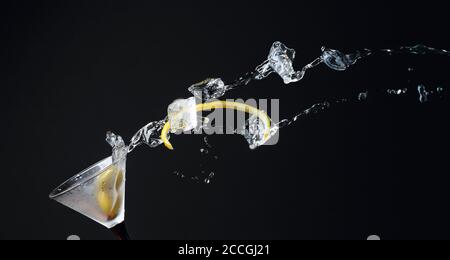 Martini mit grünen Oliven, Eis und Zitronenschale. Cocktail mit Spritzern auf schwarzem Hintergrund. Speicherplatz kopieren. Stockfoto