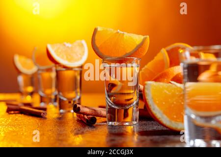 Gläser aus goldenem Tequila mit Orangenscheiben und Zimtstangen auf einem Tisch in der Bar. Selektiver Fokus. Stockfoto